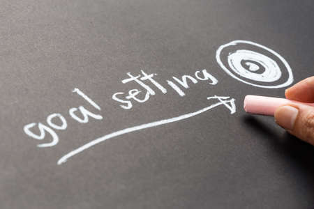 Closeup hand writing text Goal Setting with drawing arrow and target on chalkboardの写真素材
