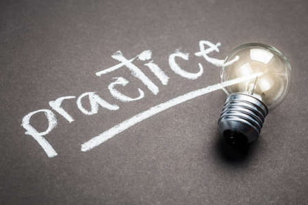 Handwriting of practice word on chalkboard with small glowing light bulbの写真素材