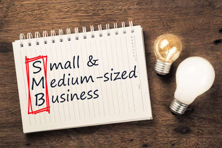 SMB or Small and Medium Sized Business text on notebook with two different light bulbsの写真素材