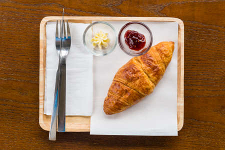 Croissant with butter and strawberry jam served on wood plate