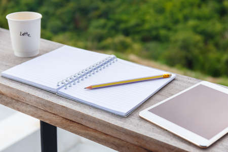 Opened notebook with cup of coffee and tablet, prepare to write at the balcony by the forest view environmentの写真素材