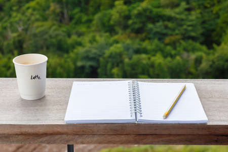 Opened notebook with pencil and cup of coffee, prepare to write at the balcony with green forest on backgroundの写真素材