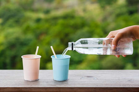 Two plastic cups of drinking cold water in the garden with hand pouring from the bottleの写真素材
