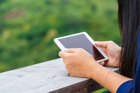 Closeup woman's hand use tablet by horizontal, blurred green forest on background