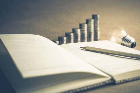 Idea for writing to make money, closeup pencil on notebook with light bulb and coins stairの写真素材