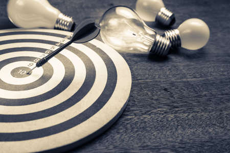 Dart hit on the center of dartboard with glowing light bulbsの写真素材