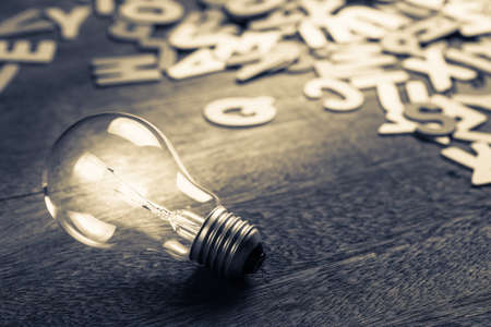 Glowing light bulb with scattered wood letters on background, finding inspiration idea concept