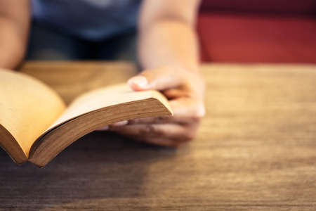 Closeup woman stretch her arm and hold the old book to read on the wood table