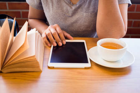 Closeup woman read tablet on the table with cup of tea and old book