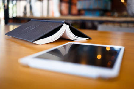 Opened book placed upside down with mobile tablet on foreground, content research, create story or leisure conceptの写真素材