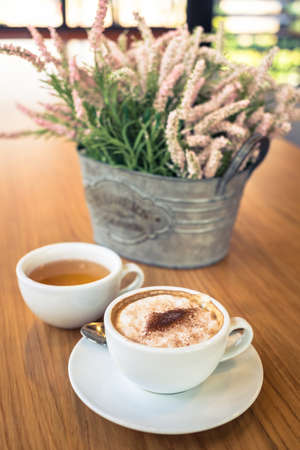 Cappuccino coffee with hot tea and flower vase on dining tableの写真素材