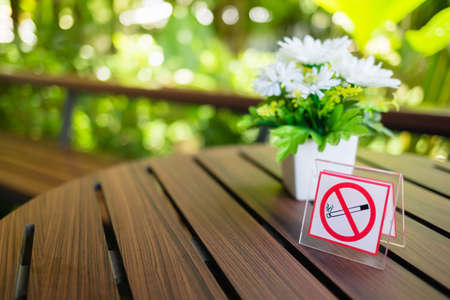 No smoking sign on the table outside the cafe with flower vase and green garden on backgroundの写真素材