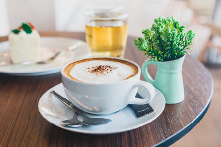 Cappuccino in white cup served on the table with decorated plant, tea water and bakeryの写真素材