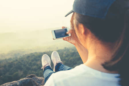 Asian woman travel to the top of the mountain and going to take picture of her feet with scenery by smartphoneの写真素材