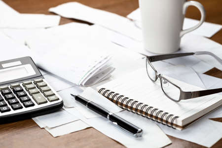 Notebook, eyeglasses and calculator on many receipts on the table