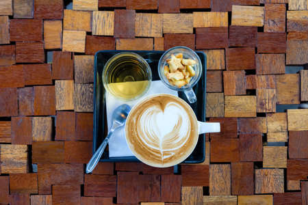 Cappuccino coffee with biscuits and tea water on cut wood pattern design of tableの写真素材