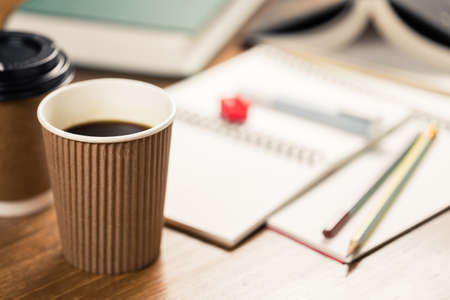 Closeup black coffee in takeaway cup on the desk with opened notebooks and booksの写真素材