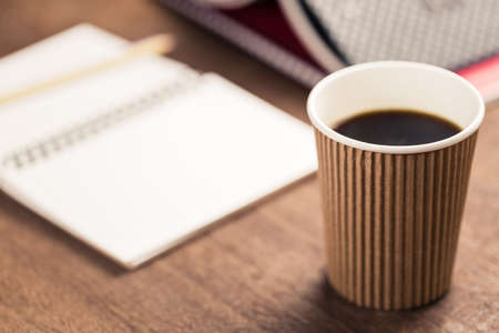 Closeup black coffee in takeaway cup on the desk with opened notebook and bookの写真素材