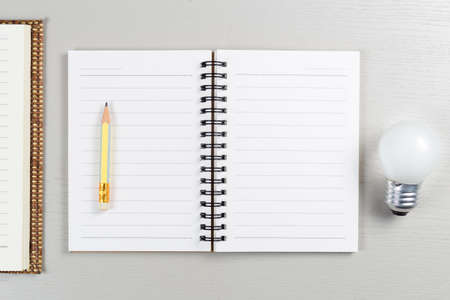 Opened small notebook with short pencil and small light bulb on gray wood table, start writing...