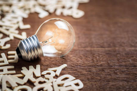 Small light bulb glowing with many English wood lettersの写真素材