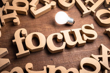 FOCUS word in scattered wood letters on the table with glowing light bulbの写真素材