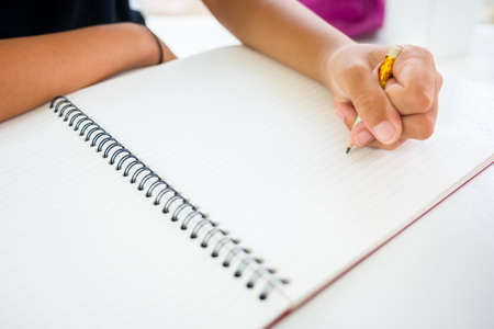 Closeup child's left hand with short pencil going to start writing or drawing something in the...