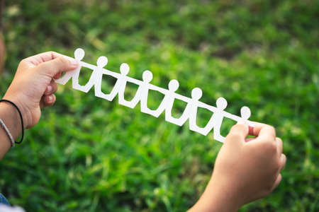 Child's hand show the success of cutting paper as a human chain doll over the green field in the...