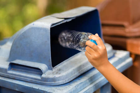Child drop the empty plastic bottle into the blue bin in the park, trash sorting by leave the...