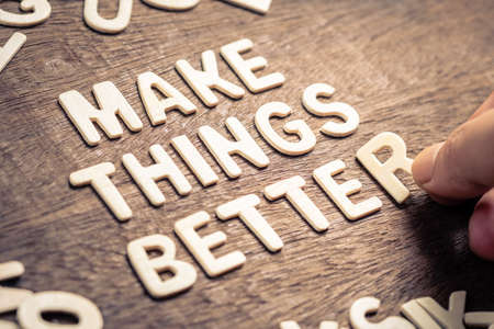 Closeup hand place the wood letters on wood table as motivation quote : MAKE THINGS BETTER