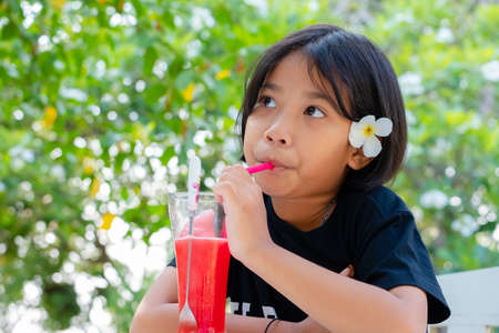 Thai child girl with plumeria flower on the ear drinking the watermelon juice in the garden