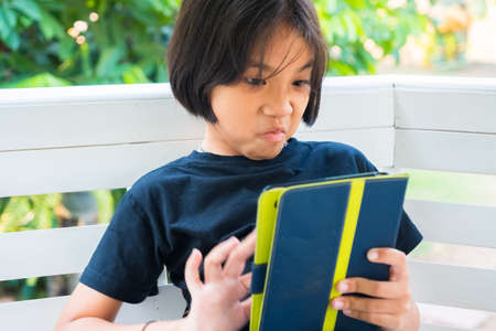 Thai child girl in angry and frustrated emotion while using the tablet in the gardenの写真素材