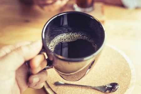 Closeup hand hold the coffee cup to drink, black drip coffee, shallow depth of field at the foam in the cupの写真素材