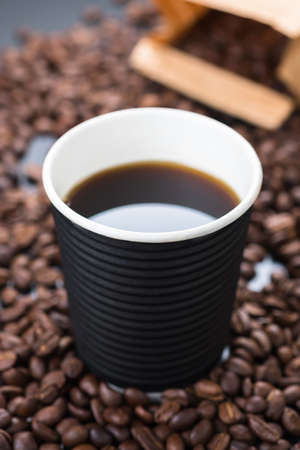 Black coffee in black biogradable cup with coffee beans and paper bag