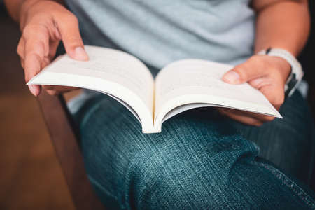 Closeup woman in casual cloths sitting on the chair and rest the book on her lap to read
