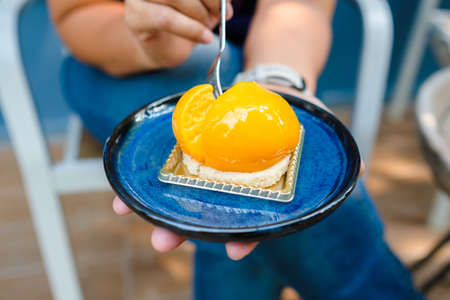 Closeup woman going to eat the orange mousse cake from the ceramic plate in her hand