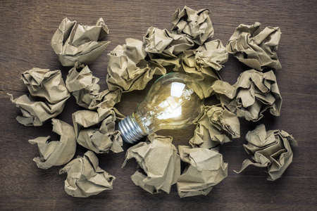 Light bulb glowing in the group of crumpled brown paper ballsの写真素材