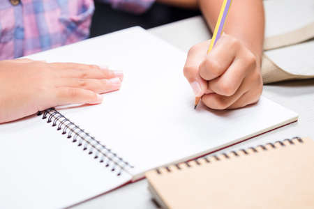 Closeup child going to write or draw something on notebook, child doing homework on the desk