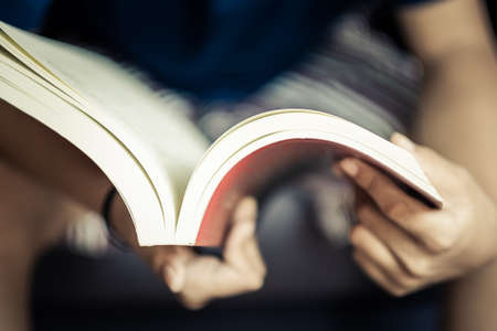 Closeup child sitting on the chair and open the pocket book on her hand, shallow depth of field at the top of the bookの写真素材