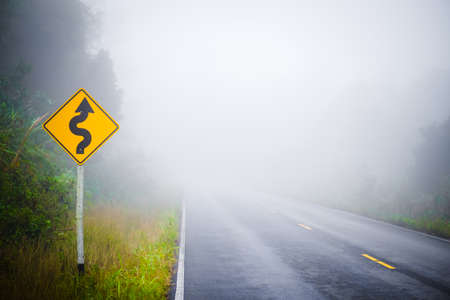Curve ahead signpost on the foggy road in the forest, winter at Phu Hin Rong Kla National Park in Thailandの写真素材