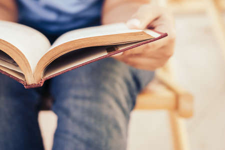 Closeup hand of woman holding old book to read while sitting on the chairの写真素材