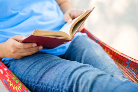 Closeup hand of woman holding old book to read while laying in the hammockの写真素材