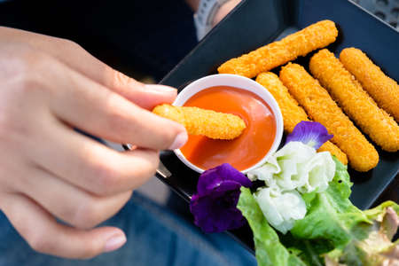 Closeup hand dip the fried chicken sticks in chili sauce to eat