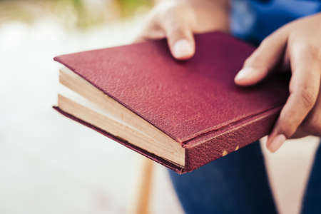 Closeup old red hardcover book in woman's hands, reading story of old novel