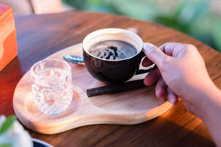 Closeup woman's hand going to take black coffee in the black cup to drink, coffee in the cafe with...