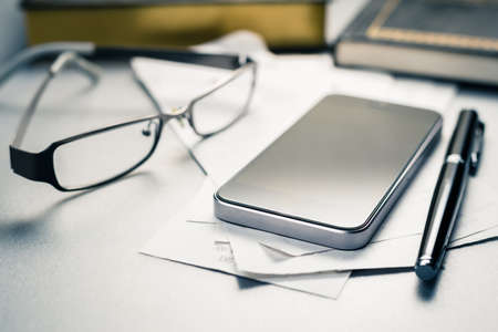 Mobile phone on bills on the desk with eyeglasses, smart phone for payment or calculation, tax conceptの写真素材