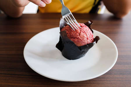 Closeup woman use the fork to eat red velvet muffin on white plateの写真素材