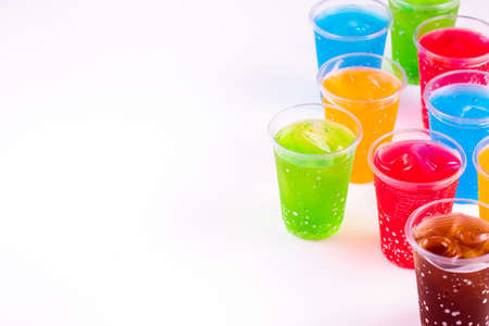 Colorful soft drinks in plastic cups on white background, many kinds and color of sweet cold drinks on the side of frame with copy spaceの写真素材