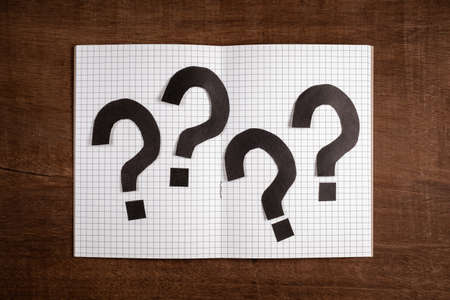 Many question marks by cut paper placed on opened notebook