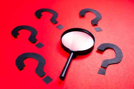Magnifying glass with many question mark symbol on red paperの写真素材