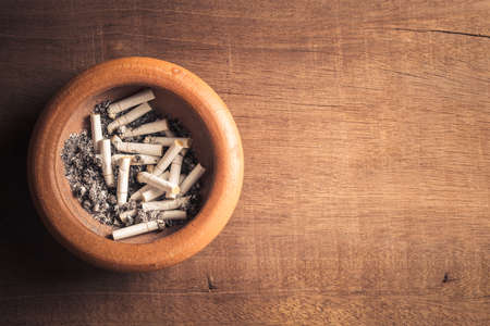 Closeup many cigarette butts with ash in the clay ashtray on wood tableの写真素材